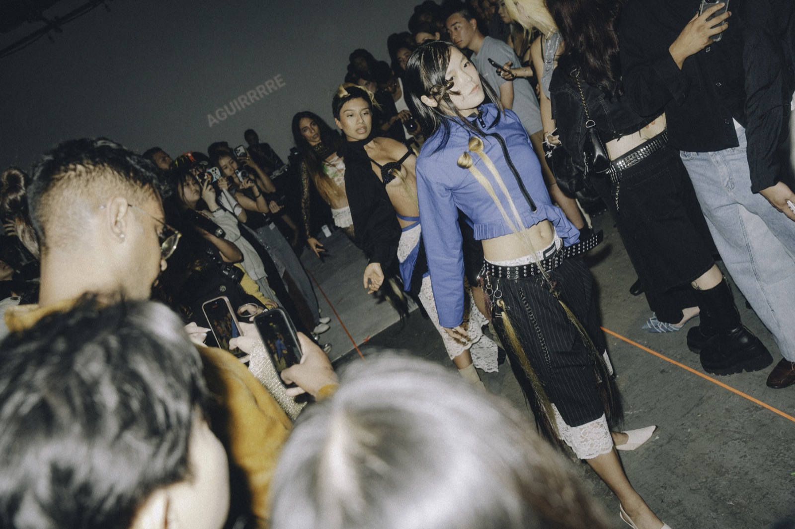 A model in a denim jacket passes close through the packed crowd.