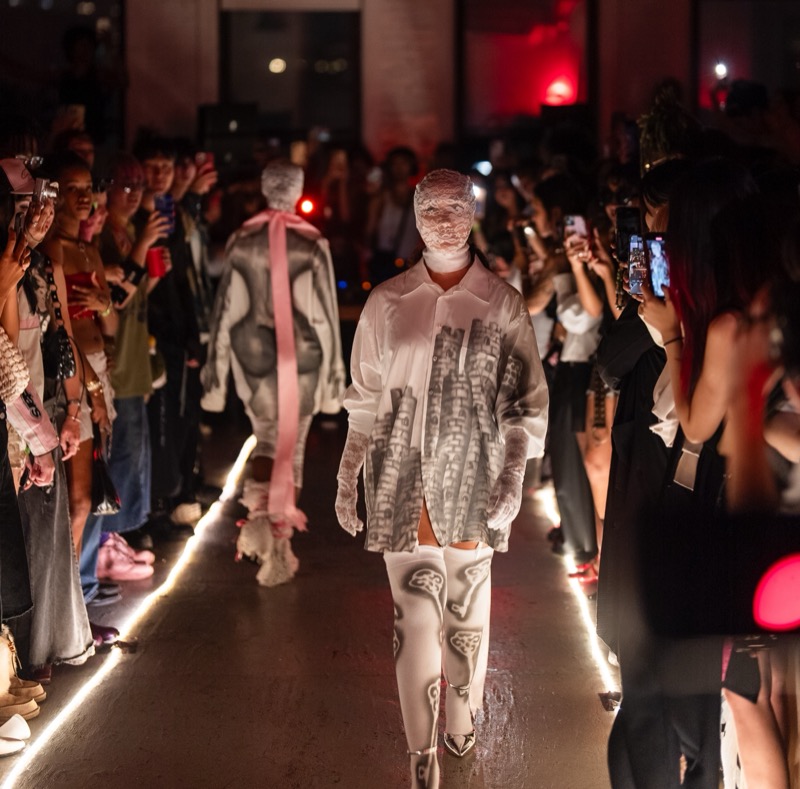 Models walk a runway outlined by glowing floor lights through a packed crowd.