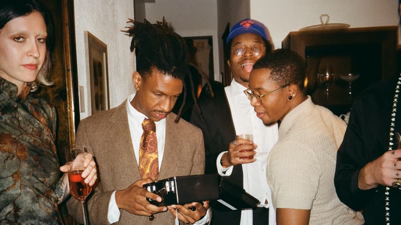 Guests in suits crowd around a player opening a black case in the castle hallway.