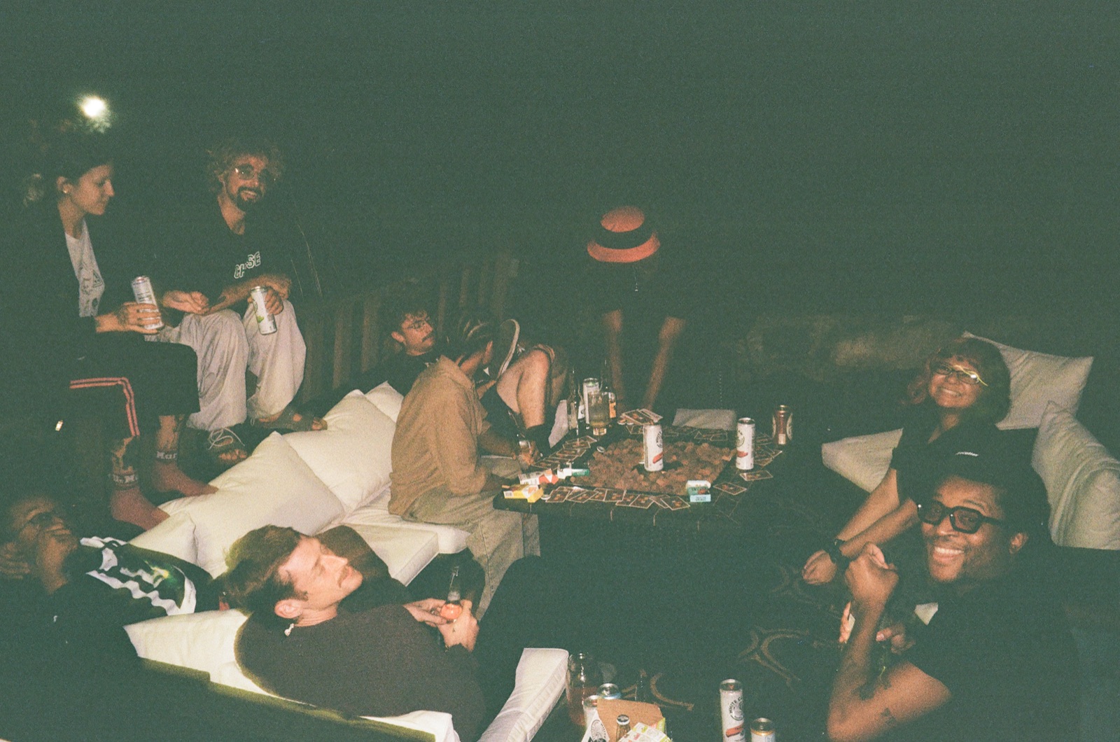 Players lounge on white sofas around a low table of drinks, late at night.